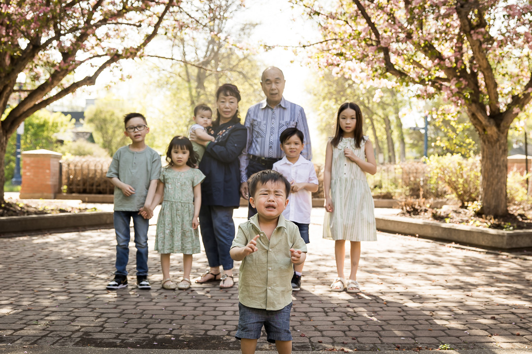Grandparents with grandchildren for outdoor family photo portraits with one grandson unhappy by Paper Bunny Studios