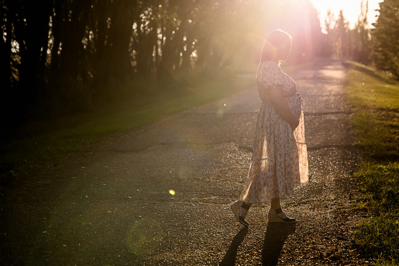 Dusk photo of mom walking cradling bump by Edmonton maternnity photographer Paper Bunny Studios