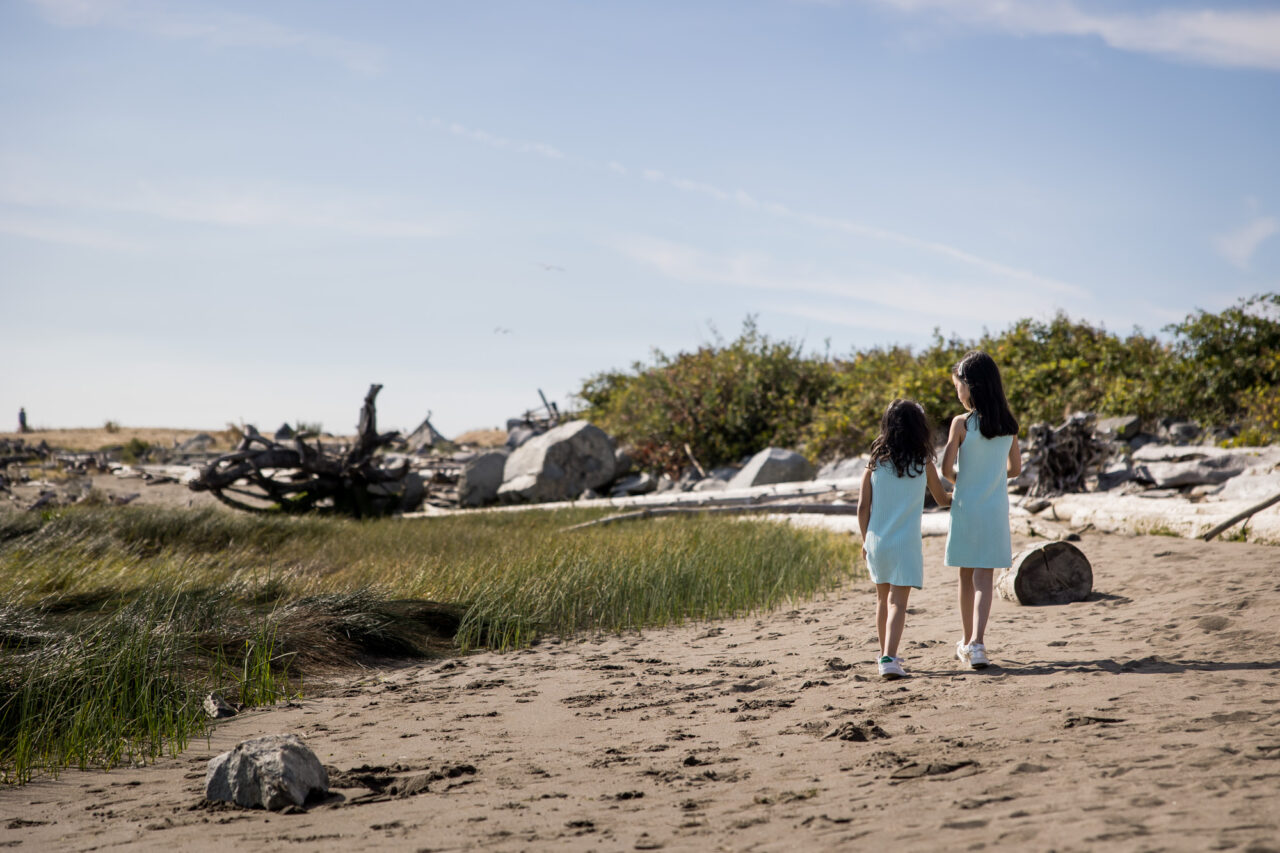 Two young girls walking on a beach in Vancouver by documentary family photographer Paper Bunny Studios