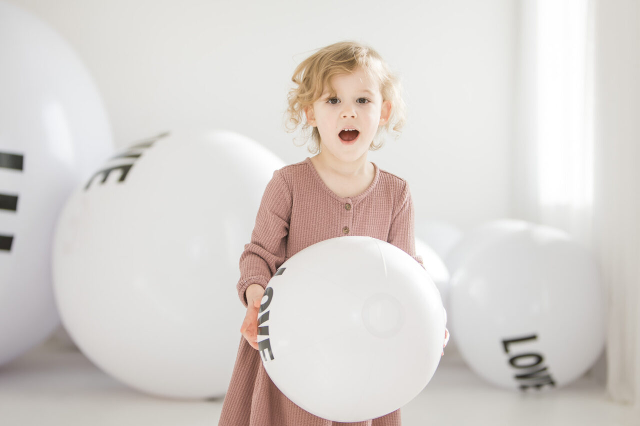 Young girl with LOVE beach ball during LOVE mini session with Paper Bunny Studios using giant beach balls saying LOVE on them as a backdrop. Image copyright Paper Bunny Studios