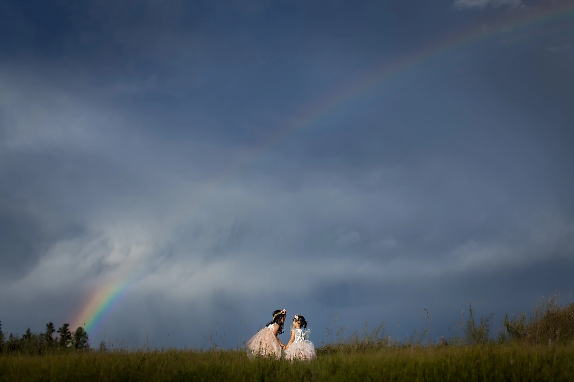 Little girls in frilly dresses playing in a field with a rainbow in the sky by Paper Bunny Studios, Edmonton family photographer